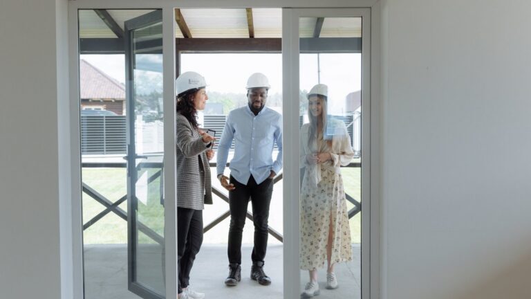 Three professionals in hard hats discussing home features during a house tour