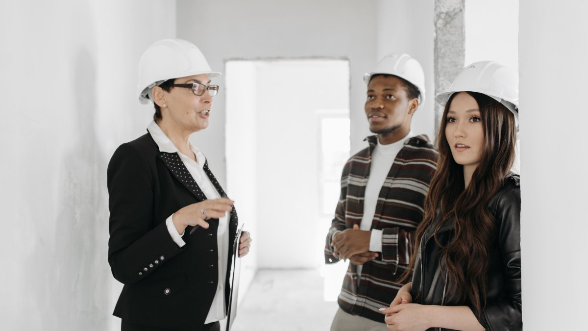 Real estate agent talks to clients at an unfinished apartment wearing helmets